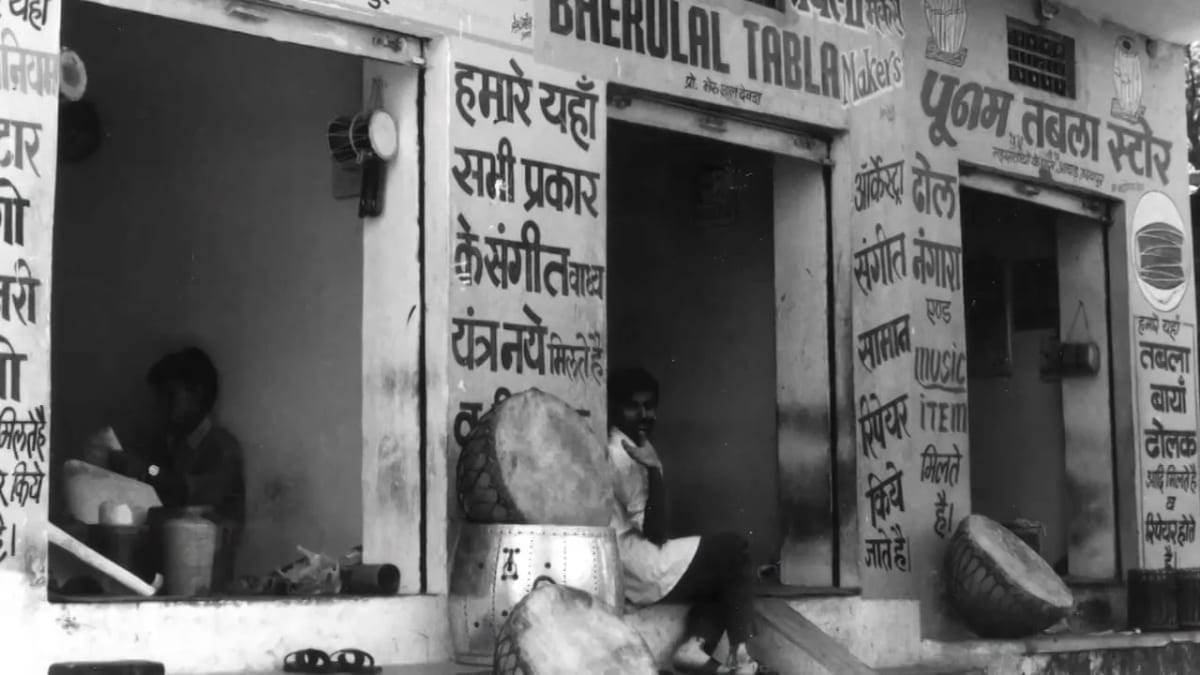 A black and white shopfront in India lettered in Hindi, tabla shells stacked on the pavement outside.